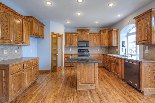 kitchen featuring a center island, brown cabinets, a sink, light wood-type flooring, and black appliances