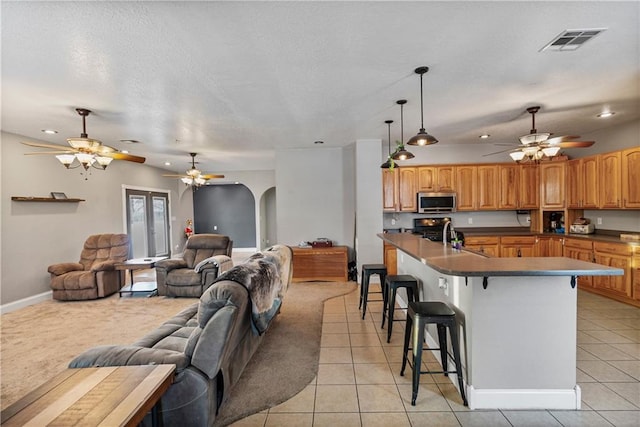 kitchen with light tile patterned flooring, appliances with stainless steel finishes, decorative light fixtures, an island with sink, and a kitchen bar