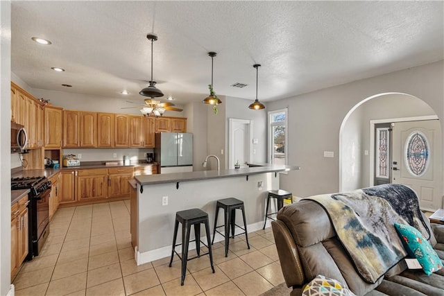 kitchen featuring a breakfast bar area, black gas stove, a center island with sink, decorative light fixtures, and white fridge