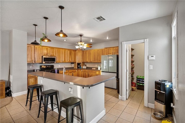 kitchen featuring black stove, a breakfast bar area, light tile patterned floors, white fridge, and a kitchen island with sink