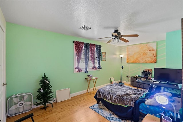 bedroom with ceiling fan, a textured ceiling, and light hardwood / wood-style floors