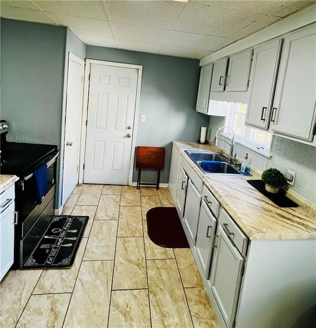 kitchen with stainless steel electric stove, sink, a paneled ceiling, and backsplash