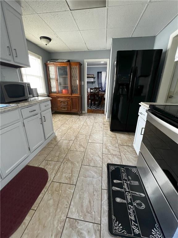 kitchen featuring white cabinetry, stove, black refrigerator with ice dispenser, and a drop ceiling