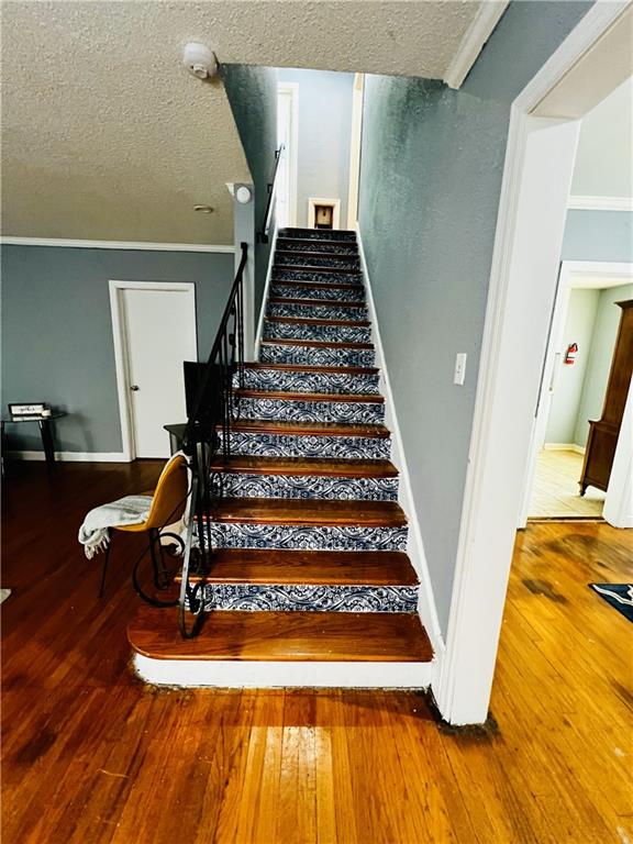 staircase with hardwood / wood-style flooring, ornamental molding, and a textured ceiling