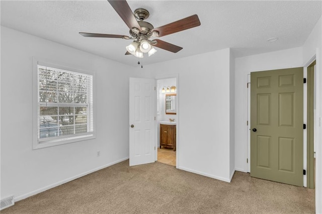 unfurnished bedroom featuring ceiling fan, light colored carpet, a textured ceiling, and ensuite bathroom