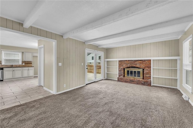 unfurnished living room featuring sink, light carpet, wooden walls, beamed ceiling, and a fireplace