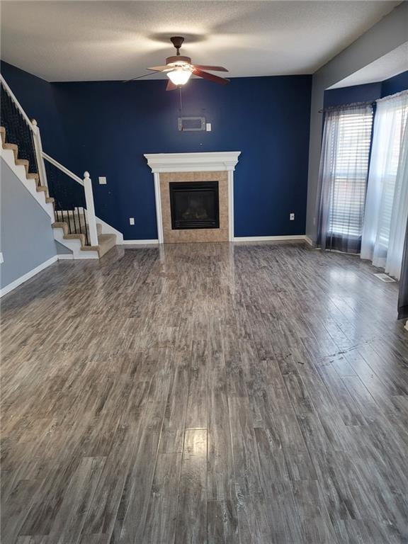 unfurnished living room featuring a tiled fireplace, a textured ceiling, wood-type flooring, and ceiling fan