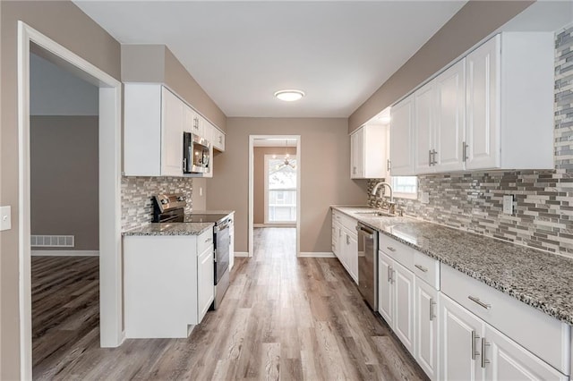 kitchen with stainless steel appliances, light stone countertops, sink, and white cabinets