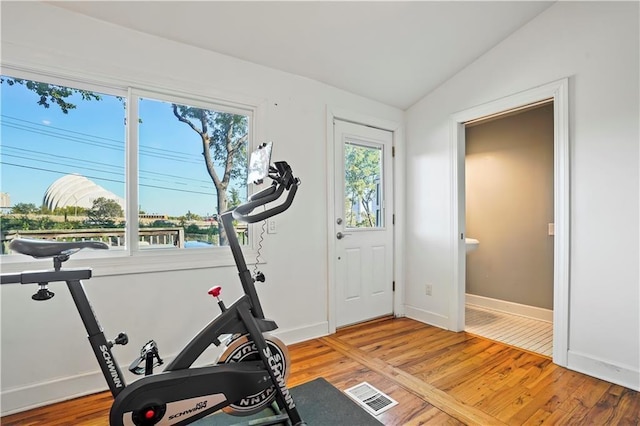 exercise room with light wood-type flooring, visible vents, vaulted ceiling, and baseboards