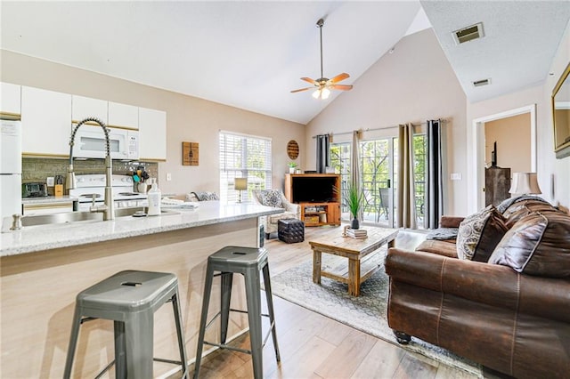 living room with high vaulted ceiling, ceiling fan, and light hardwood / wood-style flooring