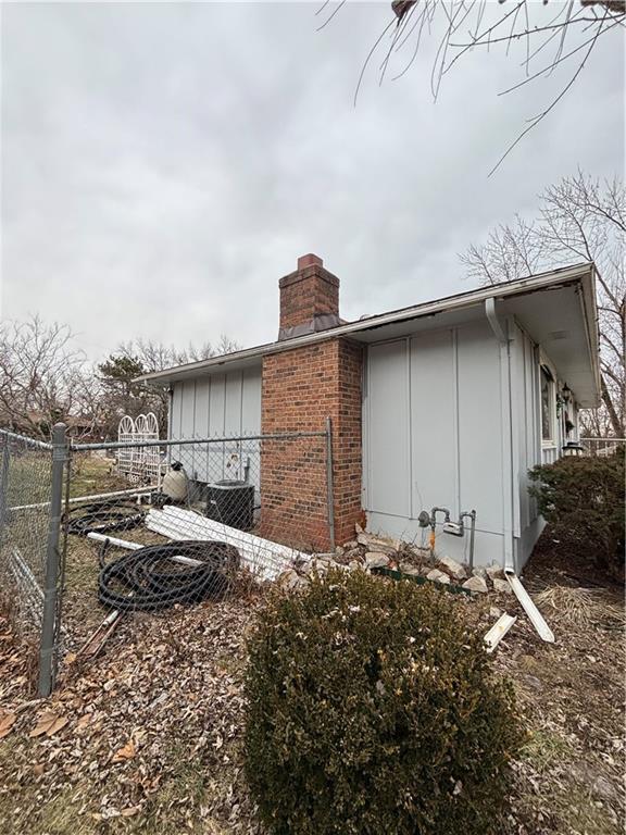 view of side of property featuring board and batten siding, brick siding, fence, and a chimney