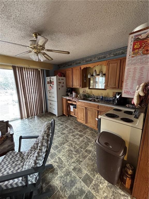 kitchen with a textured ceiling, ceiling fan, a sink, freestanding refrigerator, and brown cabinets