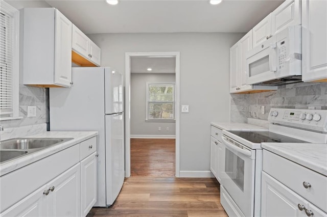 kitchen with sink, white appliances, light hardwood / wood-style flooring, backsplash, and white cabinets