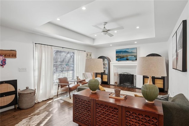 living room with ceiling fan, a raised ceiling, and hardwood / wood-style floors