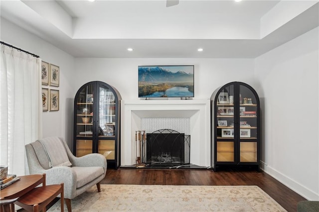 living area with a tray ceiling, dark hardwood / wood-style floors, and a tile fireplace