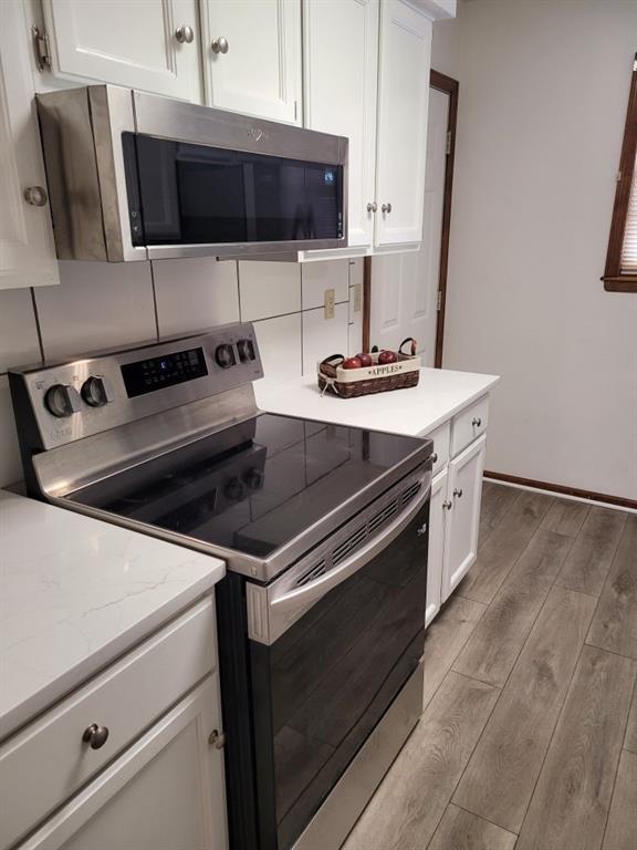 kitchen featuring light hardwood / wood-style flooring, white cabinetry, stainless steel appliances, light stone counters, and tasteful backsplash