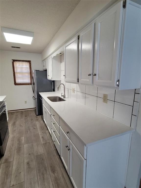 kitchen featuring sink, stove, light hardwood / wood-style floors, white cabinets, and decorative backsplash