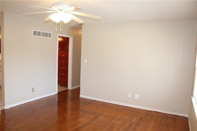 spare room with a ceiling fan, visible vents, dark wood finished floors, and baseboards