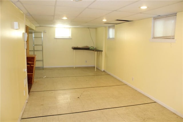 basement featuring a paneled ceiling, light floors, and baseboards