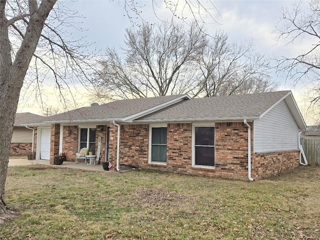 ranch-style house with a front yard, brick siding, an attached garage, and roof with shingles