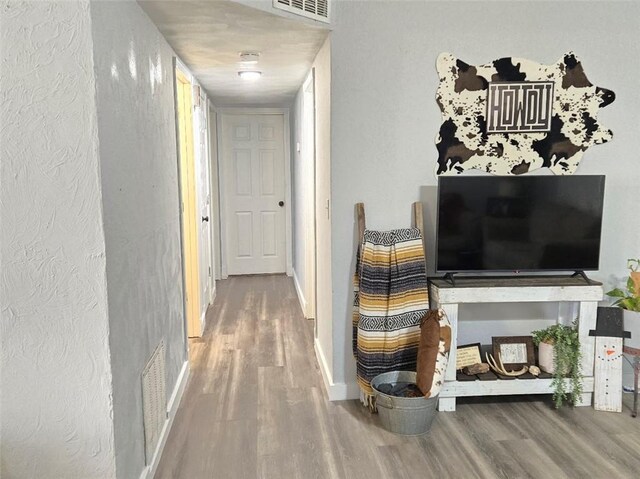 hall featuring visible vents, baseboards, and wood finished floors