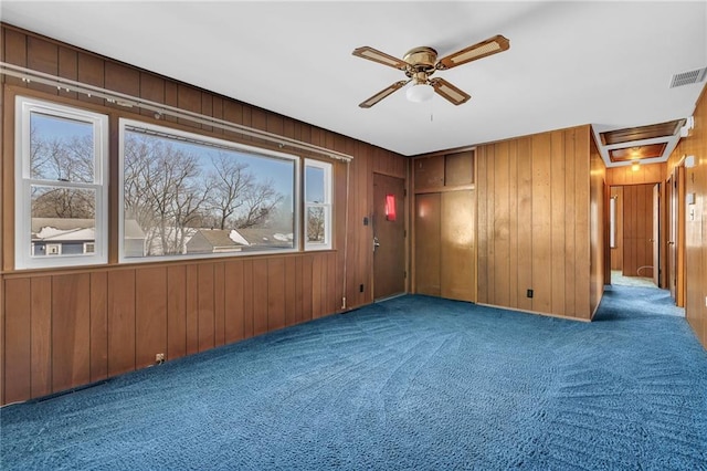 carpeted empty room featuring ceiling fan, visible vents, and wooden walls