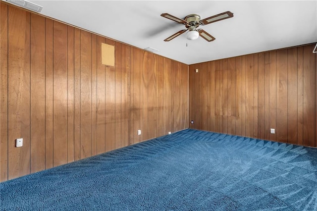 empty room featuring a ceiling fan, carpet flooring, and wooden walls