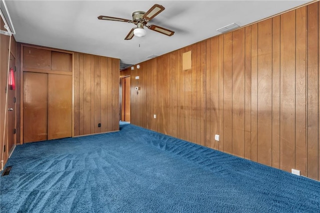 carpeted spare room featuring visible vents, ceiling fan, and wooden walls