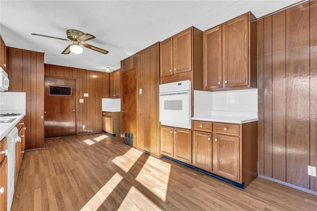 kitchen with brown cabinetry, white appliances, light countertops, and light wood-style floors