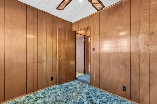 carpeted spare room featuring wood walls, ceiling fan, and a textured ceiling