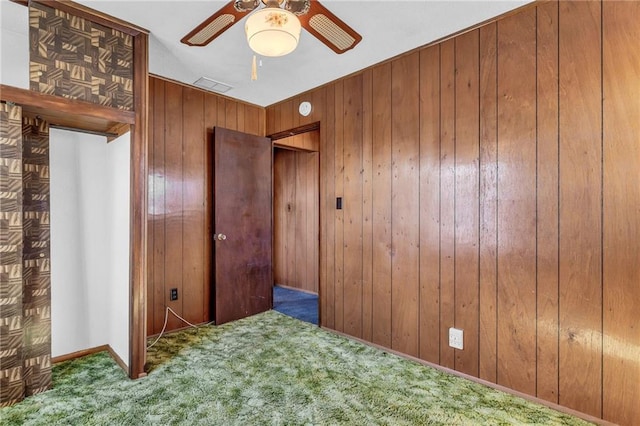 unfurnished bedroom with ceiling fan, carpet floors, wood walls, and visible vents