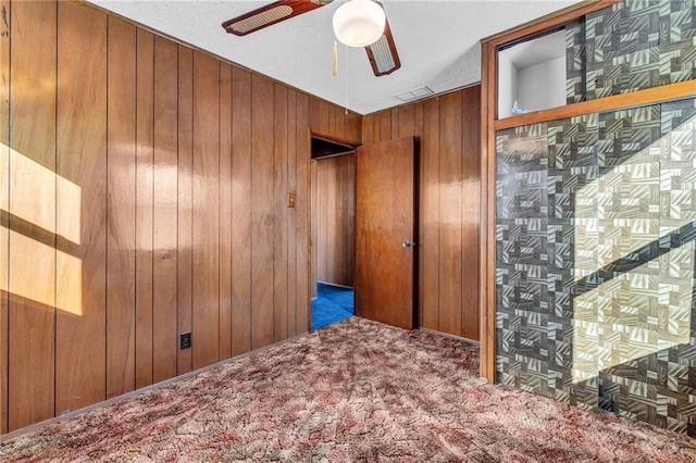 unfurnished room with visible vents, carpet flooring, ceiling fan, and wooden walls