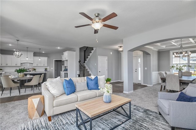 carpeted living room with coffered ceiling, ceiling fan with notable chandelier, and beam ceiling