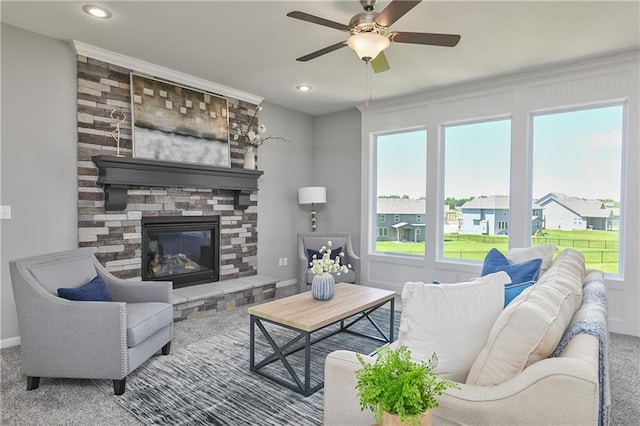 carpeted living room with a stone fireplace and ceiling fan