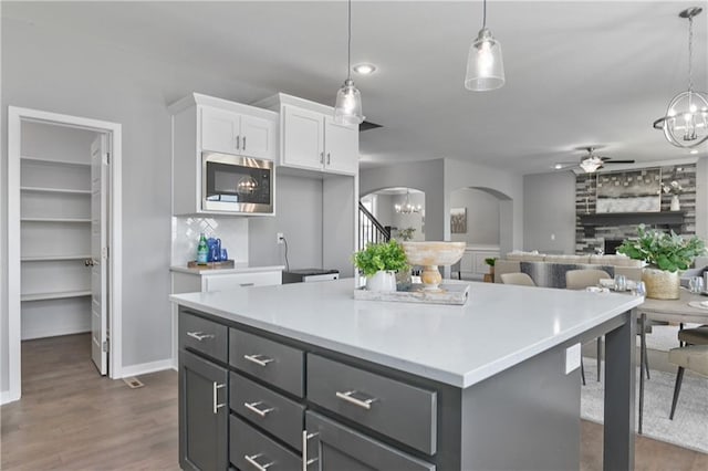 kitchen with hanging light fixtures, a center island, stainless steel microwave, white cabinets, and ceiling fan with notable chandelier