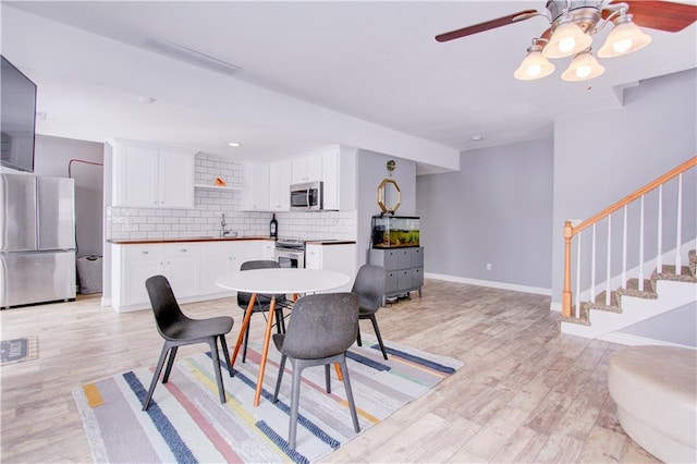 dining space with light wood-style floors, ceiling fan, stairs, and baseboards