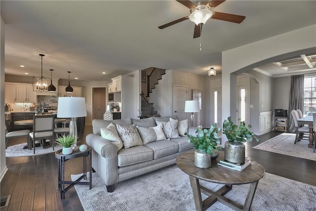 living room featuring crown molding, dark wood-type flooring, and ceiling fan with notable chandelier