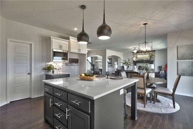 kitchen with a kitchen island, stainless steel microwave, decorative light fixtures, white cabinets, and dark hardwood / wood-style flooring