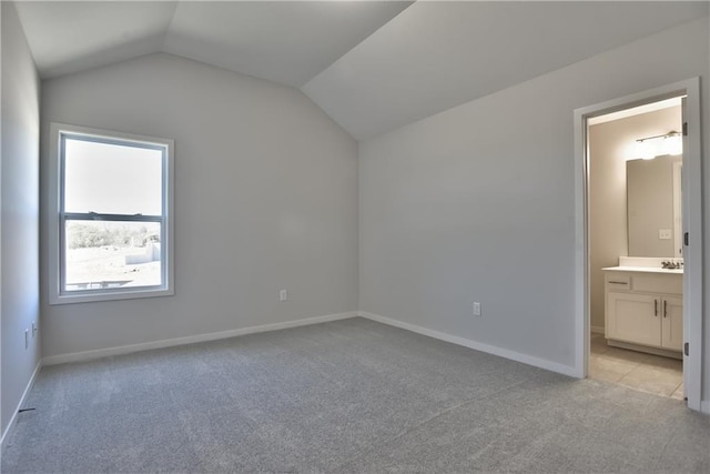 unfurnished bedroom with vaulted ceiling, light colored carpet, and ensuite bathroom