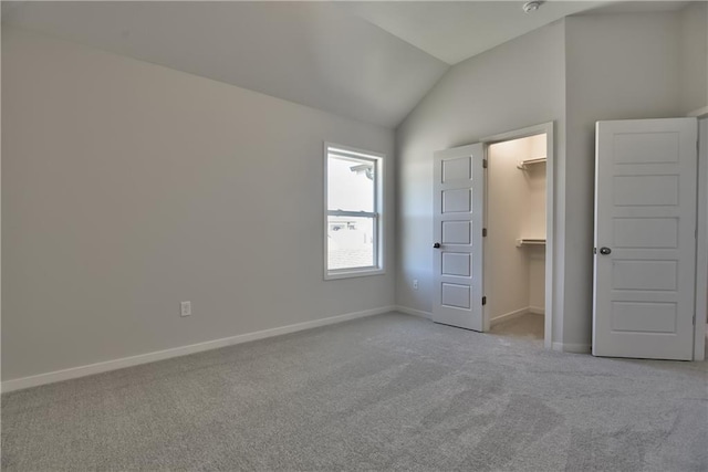 unfurnished bedroom featuring a closet, a spacious closet, vaulted ceiling, and light carpet