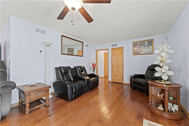 living room featuring wood-type flooring, visible vents, and ceiling fan