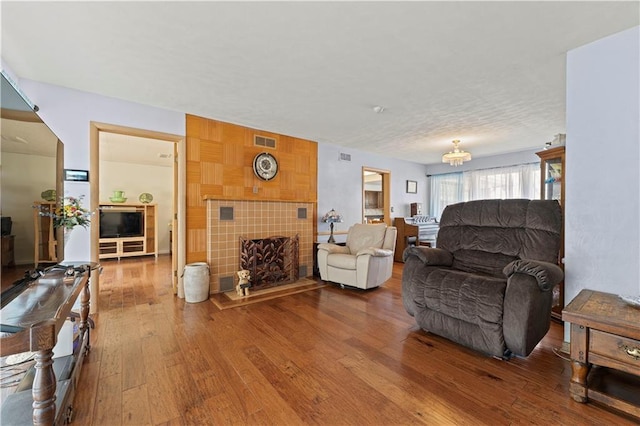 living room with wood-type flooring, visible vents, and a tiled fireplace