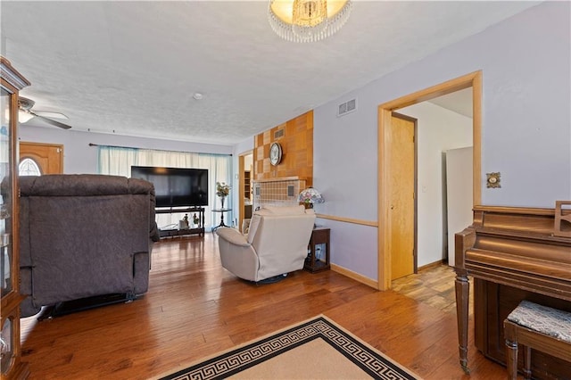 living area with a ceiling fan, visible vents, baseboards, and wood finished floors