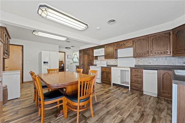 kitchen with white appliances, visible vents, backsplash, dark wood-style floors, and dark countertops