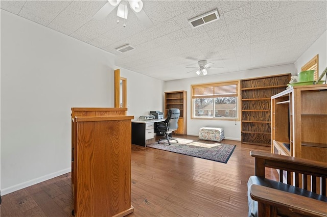 home office with a ceiling fan, visible vents, baseboards, and wood finished floors