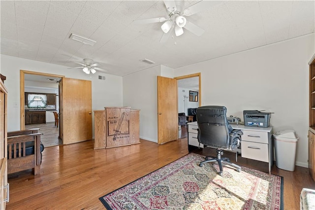 office featuring ceiling fan, light wood-type flooring, visible vents, and baseboards