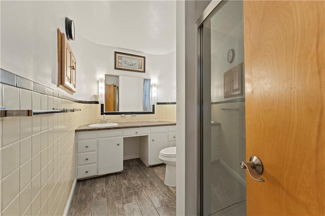 bathroom with toilet, wood finished floors, vanity, tile walls, and a shower stall