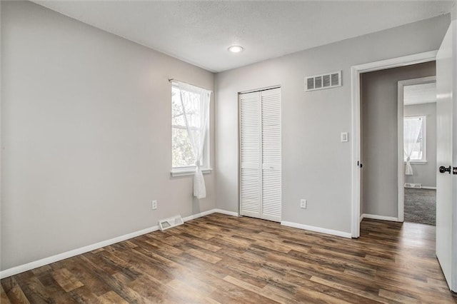 unfurnished bedroom with visible vents, baseboards, a closet, and wood finished floors