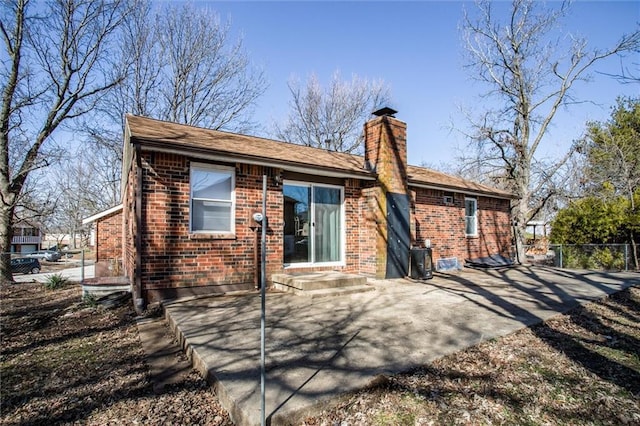 rear view of house featuring fence, brick siding, and a chimney