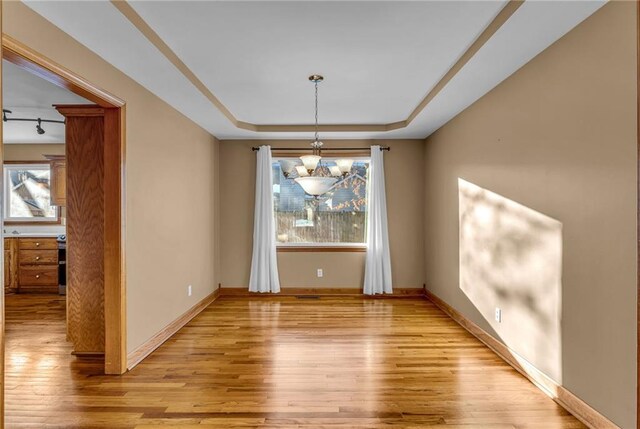 unfurnished dining area with an inviting chandelier, a raised ceiling, and light hardwood / wood-style flooring